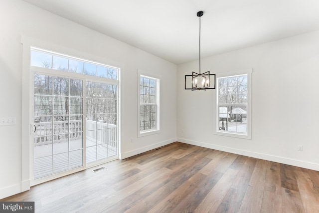 unfurnished dining area with a chandelier, wood finished floors, visible vents, and baseboards