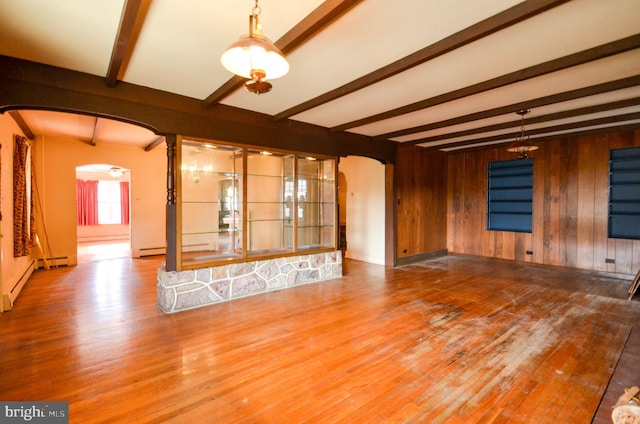 unfurnished living room featuring beamed ceiling, hardwood / wood-style floors, a baseboard heating unit, and wood walls