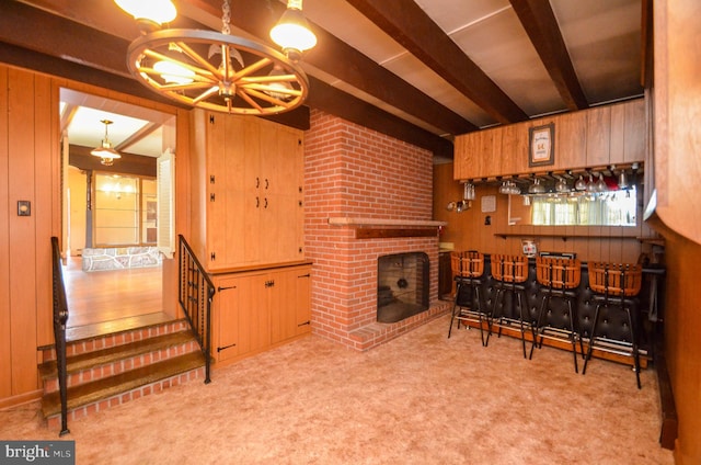 carpeted living room with beamed ceiling, indoor bar, wooden walls, and a brick fireplace