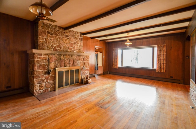 unfurnished living room with wooden walls, hardwood / wood-style flooring, baseboard heating, a fireplace, and beamed ceiling