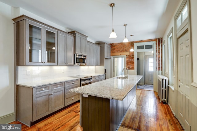 kitchen with pendant lighting, a kitchen island with sink, radiator, sink, and appliances with stainless steel finishes