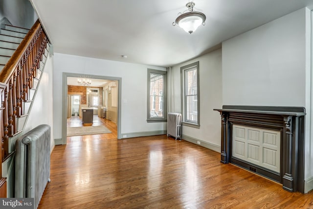 unfurnished living room featuring a chandelier, radiator heating unit, and hardwood / wood-style floors