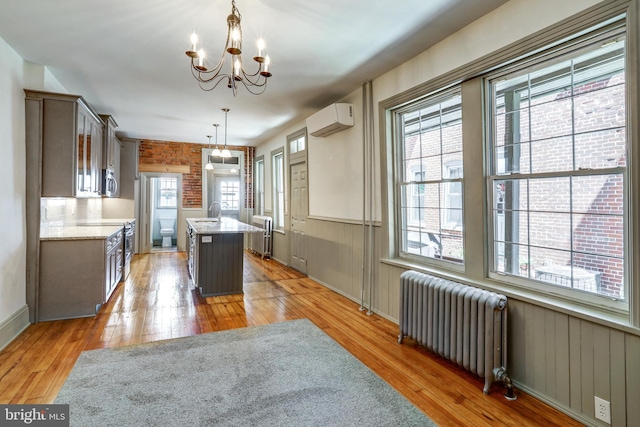 kitchen with radiator heating unit, a center island, a notable chandelier, a wall mounted AC, and pendant lighting