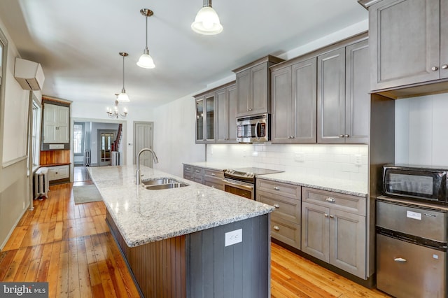 kitchen featuring sink, radiator heating unit, stainless steel appliances, an island with sink, and pendant lighting