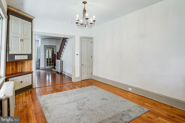 unfurnished dining area with hardwood / wood-style flooring, radiator heating unit, and an inviting chandelier