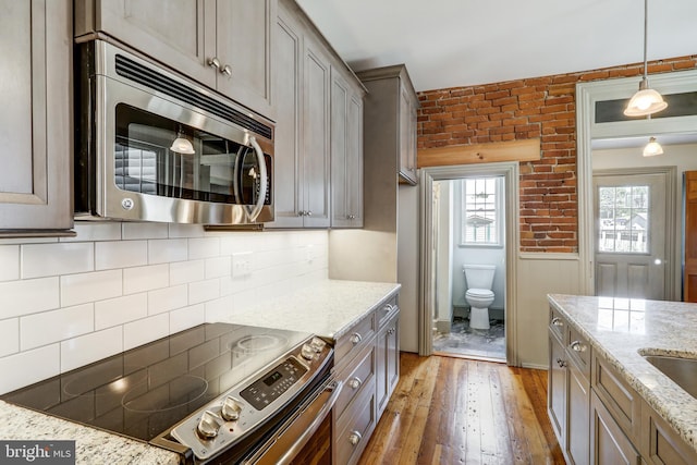 kitchen featuring light stone countertops, appliances with stainless steel finishes, dark hardwood / wood-style flooring, brick wall, and hanging light fixtures