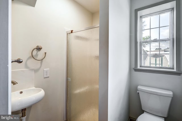 bathroom featuring toilet, a shower with shower door, and sink