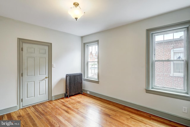 empty room featuring a healthy amount of sunlight, light wood-type flooring, and radiator