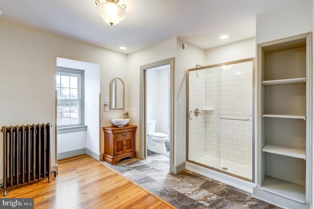 bathroom with radiator, toilet, vanity, a shower with shower door, and hardwood / wood-style flooring