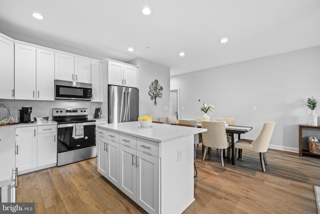 kitchen with appliances with stainless steel finishes, white cabinetry, light hardwood / wood-style flooring, and a center island