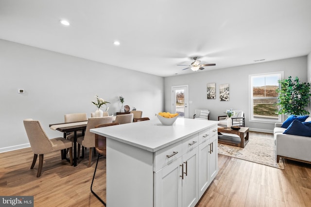 kitchen with light hardwood / wood-style flooring, a breakfast bar, a center island, ceiling fan, and white cabinets