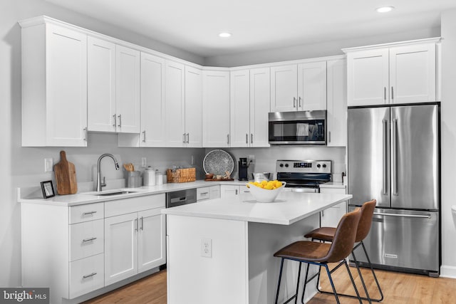 kitchen featuring stainless steel appliances, a center island, sink, white cabinets, and light hardwood / wood-style floors