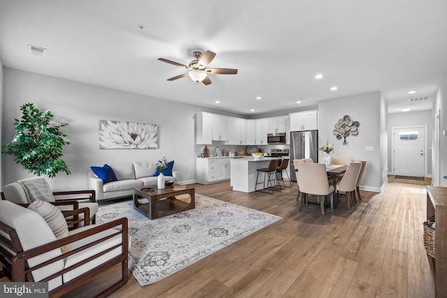 living room featuring ceiling fan, sink, and light hardwood / wood-style floors