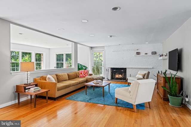 living room with light hardwood / wood-style floors, a fireplace, brick wall, and plenty of natural light