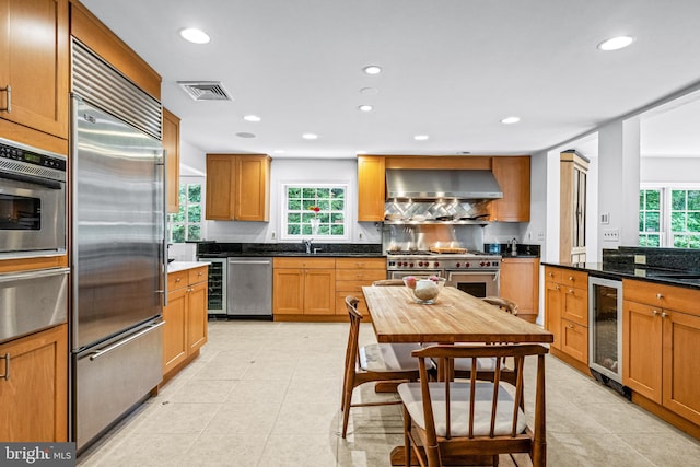 kitchen featuring light tile patterned flooring, high quality appliances, wine cooler, and wall chimney exhaust hood