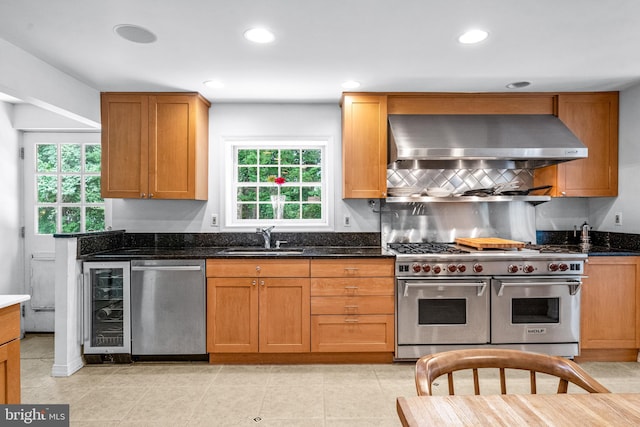 kitchen with stainless steel appliances, dark stone countertops, sink, ventilation hood, and wine cooler