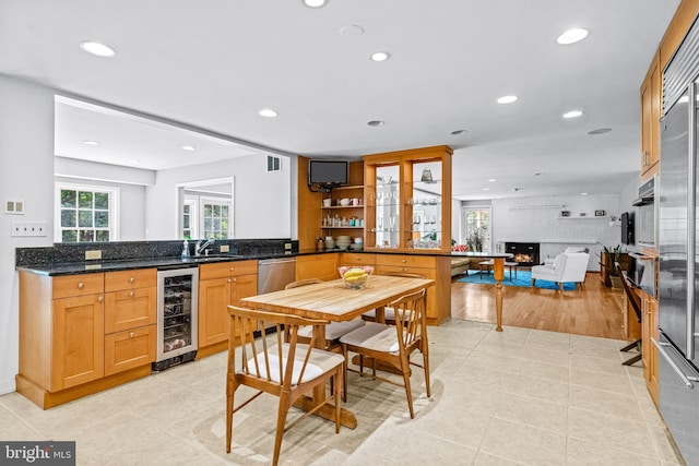 kitchen featuring sink, a fireplace, light tile patterned floors, dark stone countertops, and beverage cooler