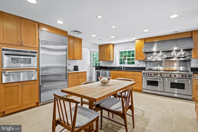 kitchen with tasteful backsplash, wall chimney range hood, sink, light tile patterned flooring, and premium appliances