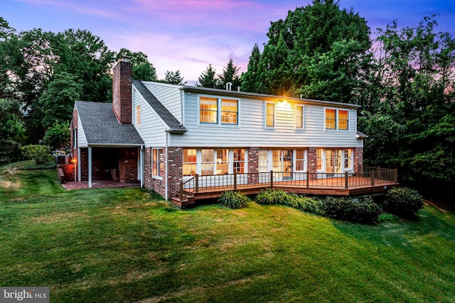 back house at dusk with a wooden deck and a lawn