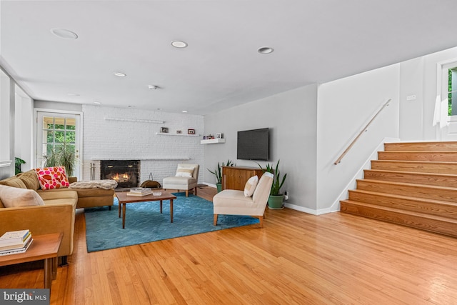 living room featuring brick wall, a fireplace, and light wood-type flooring