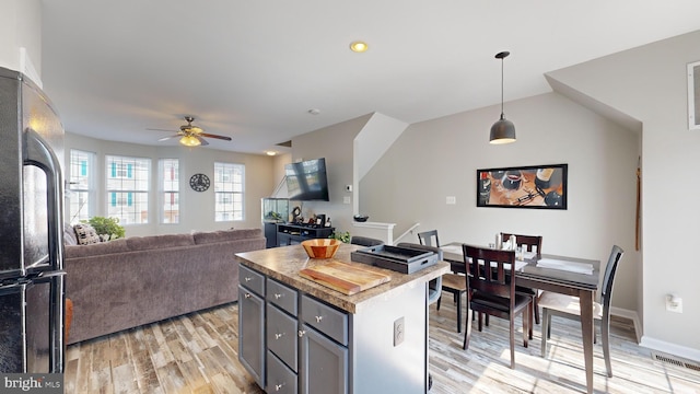 kitchen featuring refrigerator, gray cabinetry, ceiling fan, a kitchen island, and hanging light fixtures