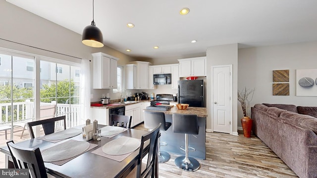 kitchen with black appliances, white cabinets, sink, decorative light fixtures, and light hardwood / wood-style floors