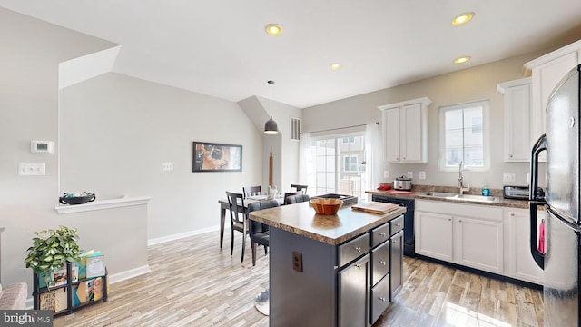 kitchen with light wood-type flooring, a kitchen island, decorative light fixtures, white cabinetry, and stainless steel refrigerator