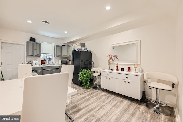 kitchen with gray cabinets, black refrigerator, light wood-type flooring, and sink