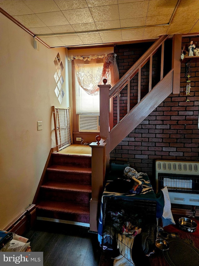 staircase featuring baseboard heating, brick wall, heating unit, cooling unit, and wood-type flooring