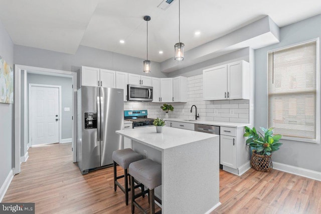 kitchen featuring decorative backsplash, appliances with stainless steel finishes, decorative light fixtures, a kitchen island, and white cabinetry