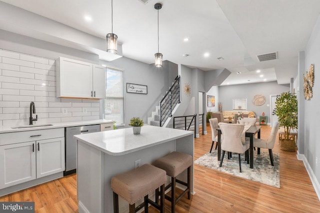 kitchen featuring backsplash, sink, stainless steel dishwasher, decorative light fixtures, and a kitchen island