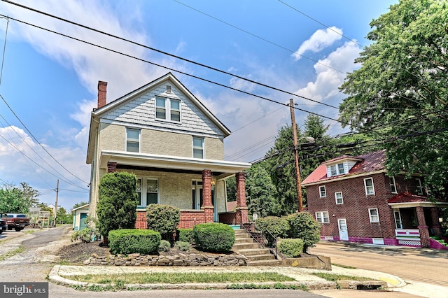 american foursquare style home with covered porch, a chimney, stucco siding, and brick siding