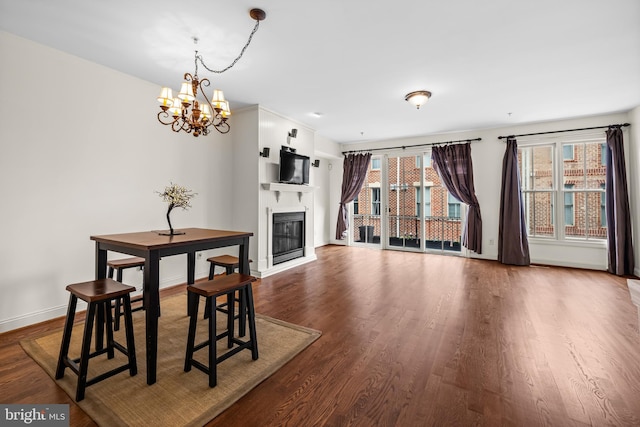 dining area with a chandelier, a glass covered fireplace, dark wood finished floors, and baseboards