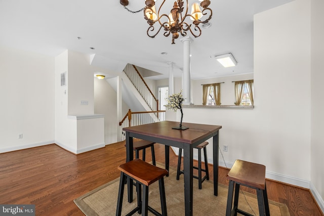 dining space featuring visible vents, baseboards, wood finished floors, stairs, and ornate columns