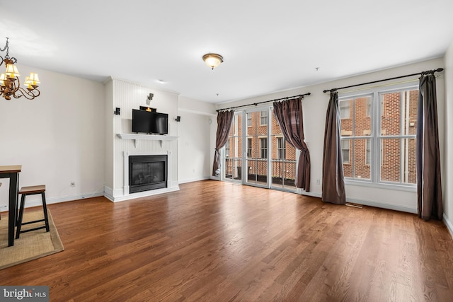 unfurnished living room featuring wood finished floors, plenty of natural light, a glass covered fireplace, and a notable chandelier