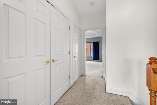 hall with baseboards and light colored carpet