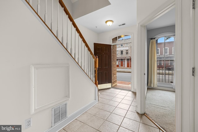 entrance foyer featuring light tile patterned flooring, visible vents, light carpet, and stairs