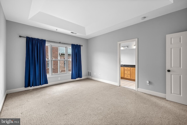 empty room with a raised ceiling, light carpet, visible vents, and baseboards