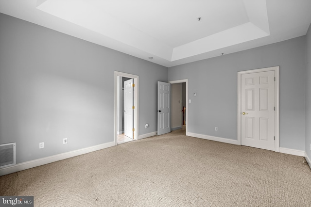 unfurnished bedroom featuring carpet floors, visible vents, a tray ceiling, and baseboards