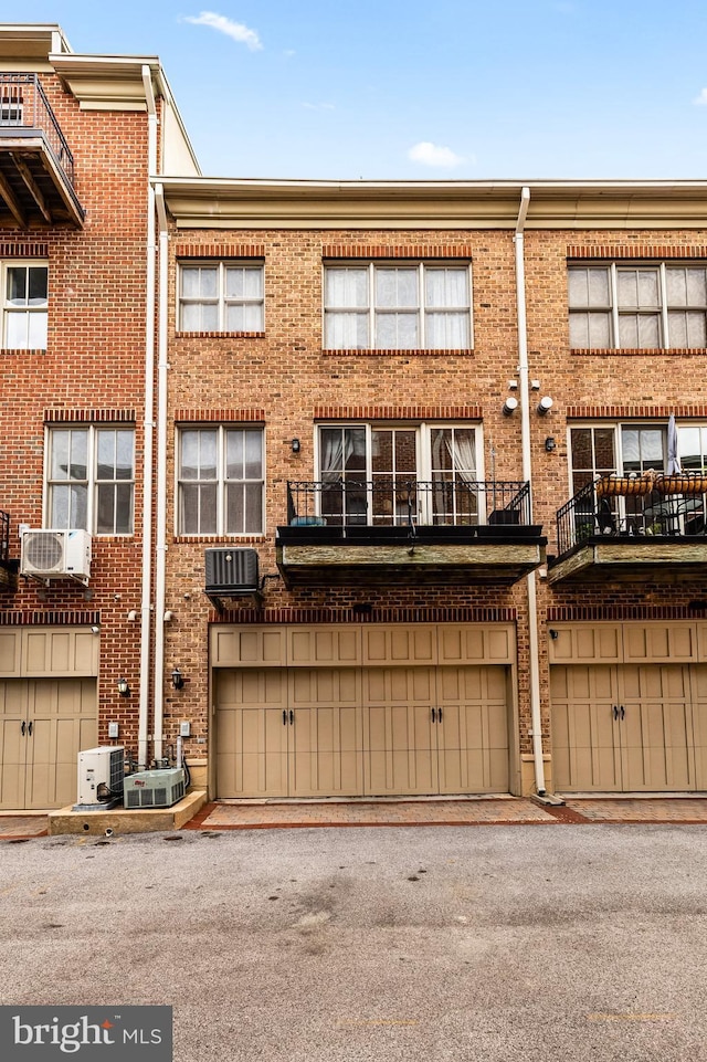 exterior space featuring ac unit, brick siding, central air condition unit, an attached garage, and cooling unit