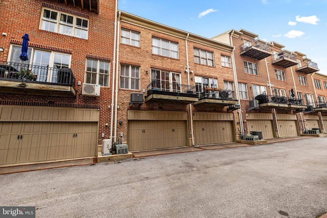 exterior space with a wall mounted air conditioner, brick siding, an attached garage, and central AC unit