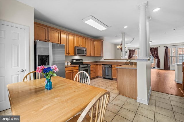 kitchen featuring light tile patterned floors, decorative columns, a peninsula, stainless steel appliances, and a sink