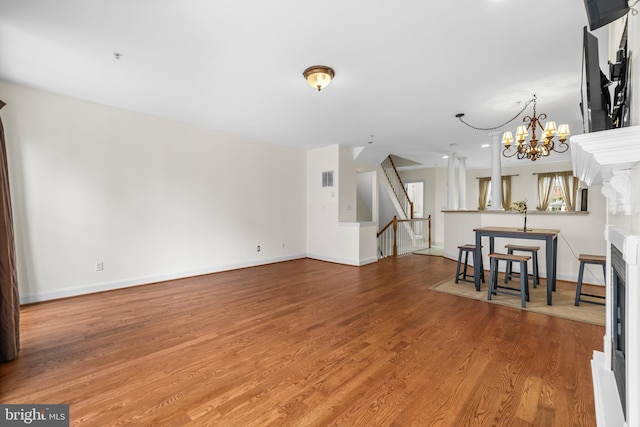 unfurnished living room with a chandelier, wood finished floors, visible vents, baseboards, and stairs