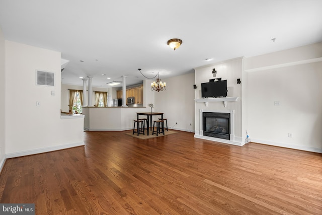 unfurnished living room featuring wood finished floors, visible vents, baseboards, a glass covered fireplace, and an inviting chandelier