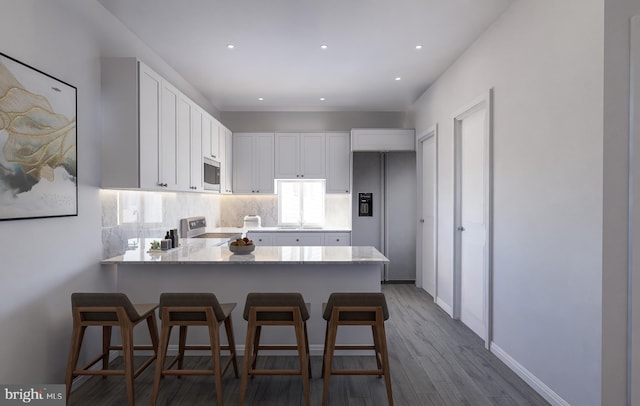 kitchen featuring dark wood-style floors, tasteful backsplash, appliances with stainless steel finishes, white cabinets, and a peninsula