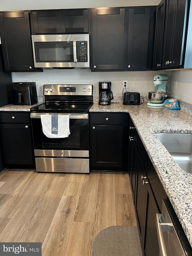 kitchen with appliances with stainless steel finishes, light hardwood / wood-style floors, and light stone counters