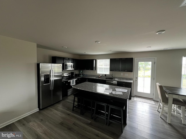 kitchen featuring stainless steel appliances, stone counters, dark hardwood / wood-style floors, a kitchen island, and a breakfast bar area