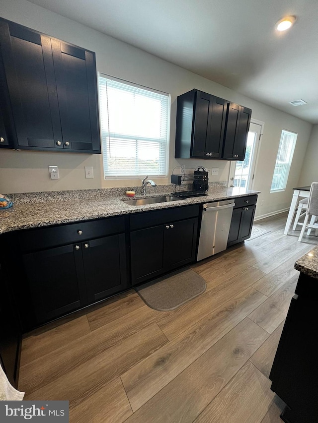 kitchen featuring light stone countertops, light hardwood / wood-style floors, stainless steel dishwasher, and sink