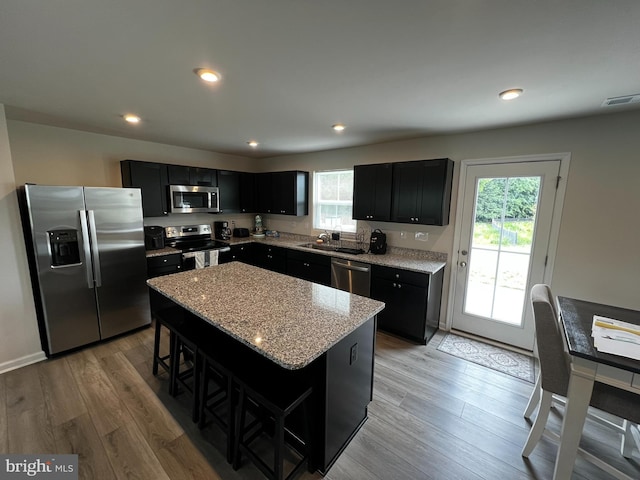 kitchen with light stone countertops, stainless steel appliances, a breakfast bar, a kitchen island, and light wood-type flooring