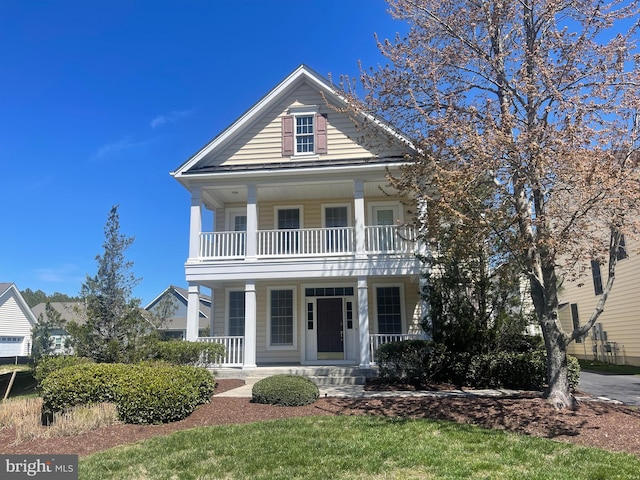 neoclassical home with a balcony, a porch, and a front yard